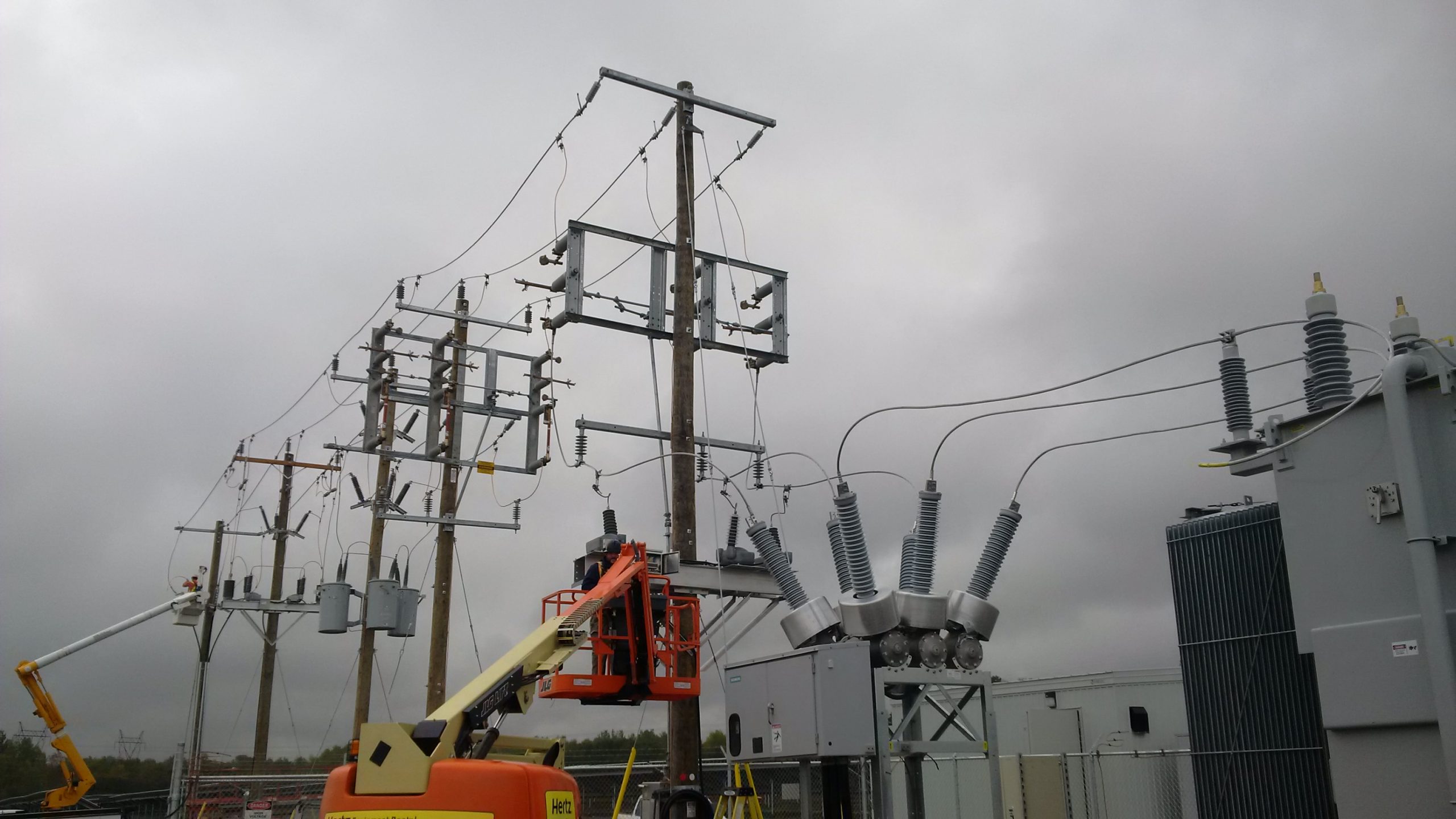 Two linesmen work from articulating man-lift in rear and telescopic boom man-lift front connecting transmission lines to HONI grid