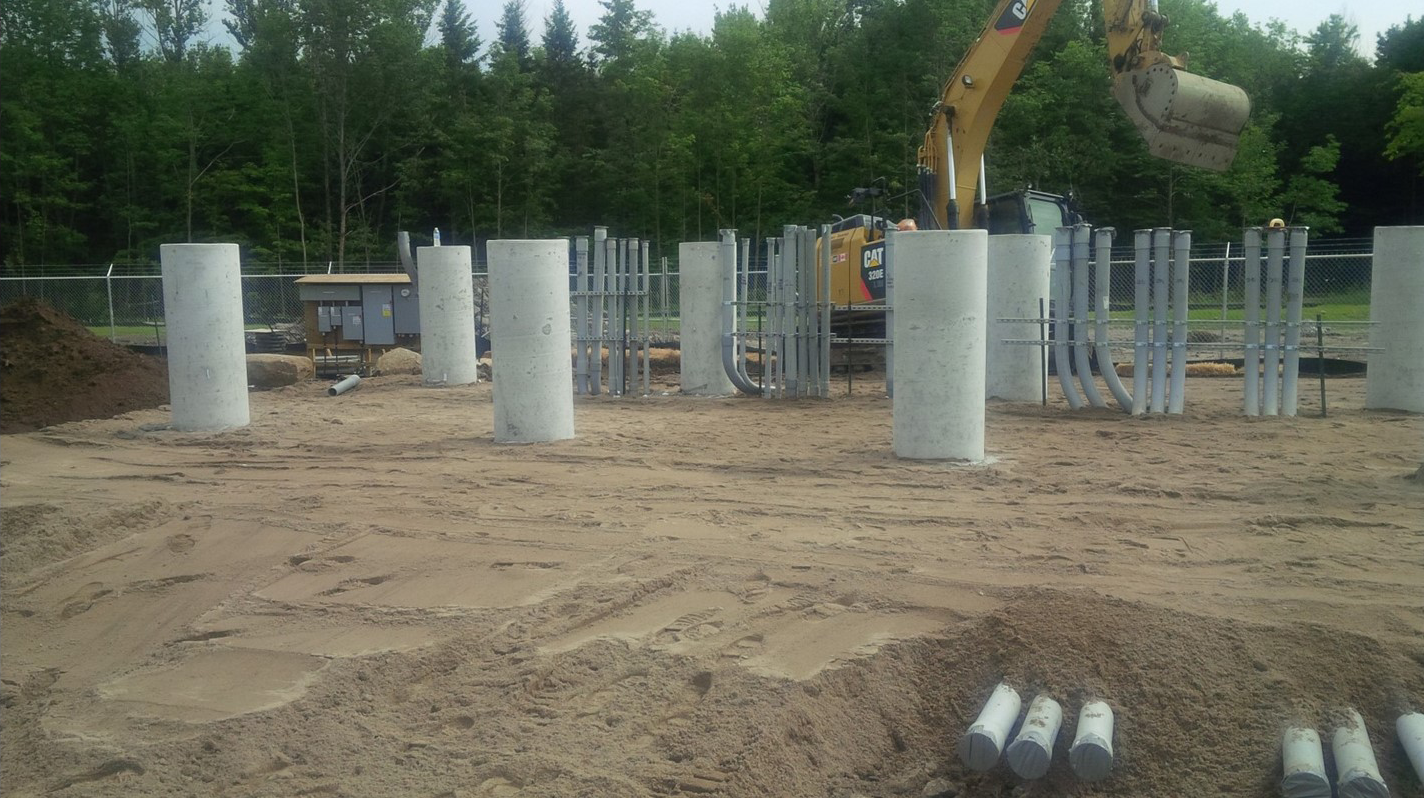 Excavator grading granular material around foundation piers and electrical conduit for a utility-scale solar substation