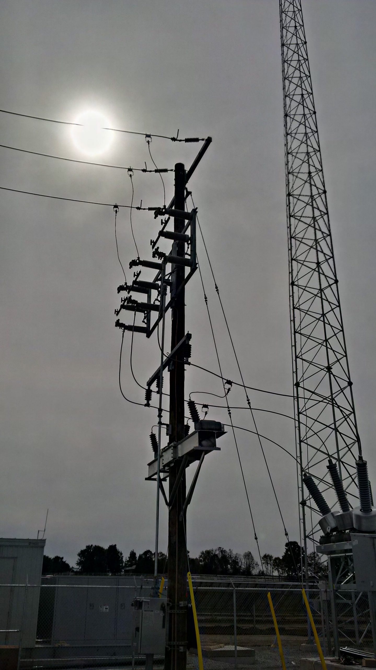 Communication Tower, main circuit breaker, line switches on hydro pole. grey sky with sun 