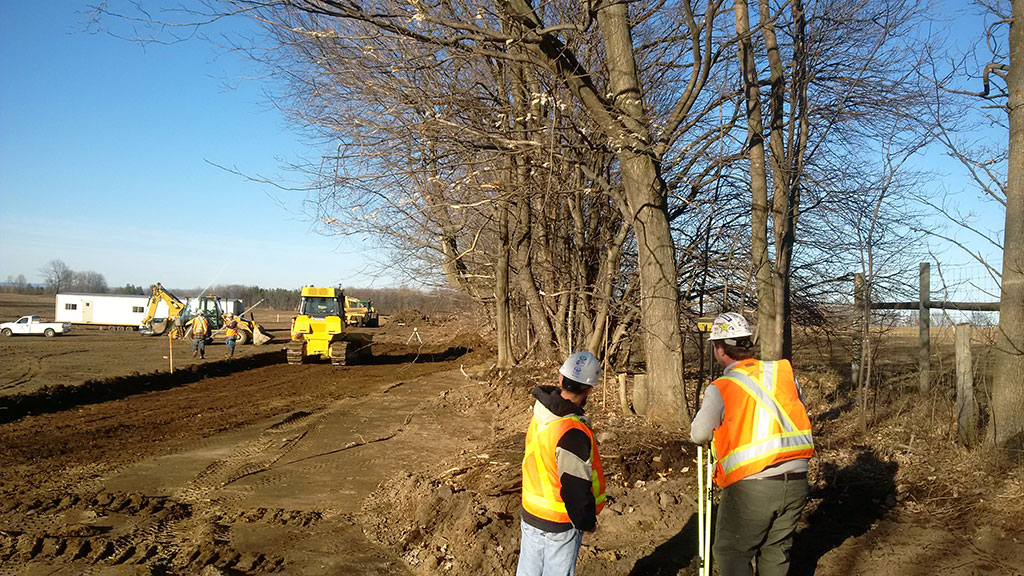 cm0512 Surveying crew install grade stakes a Bulldozer grading site and cutting a road subgrade a clear blue sky